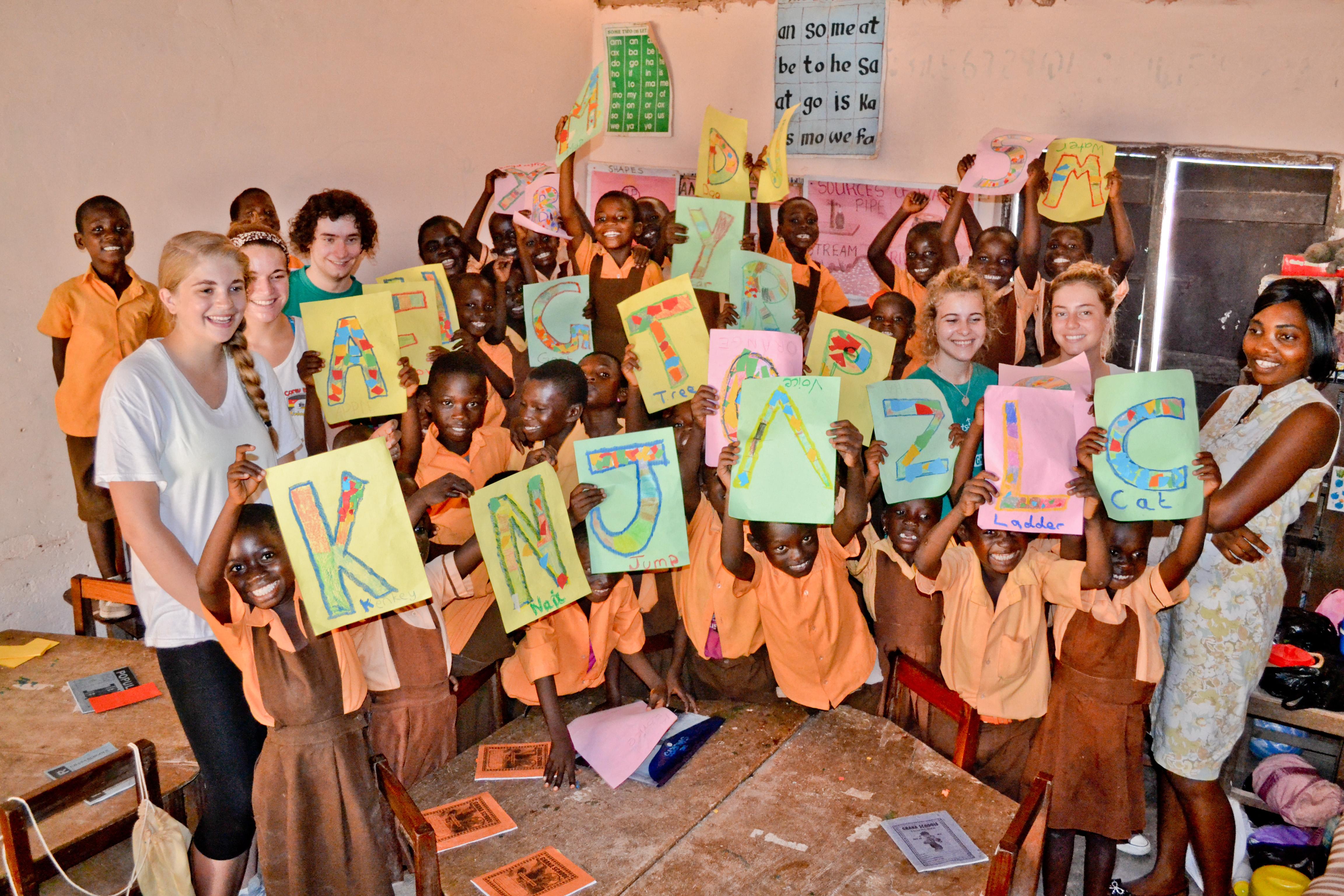 A group photo of students with their alphabet artwork with a volunteer teaching English in Ghana Projects Abroad volunteers take a group photo with their students during their teaching work experience in Ghana